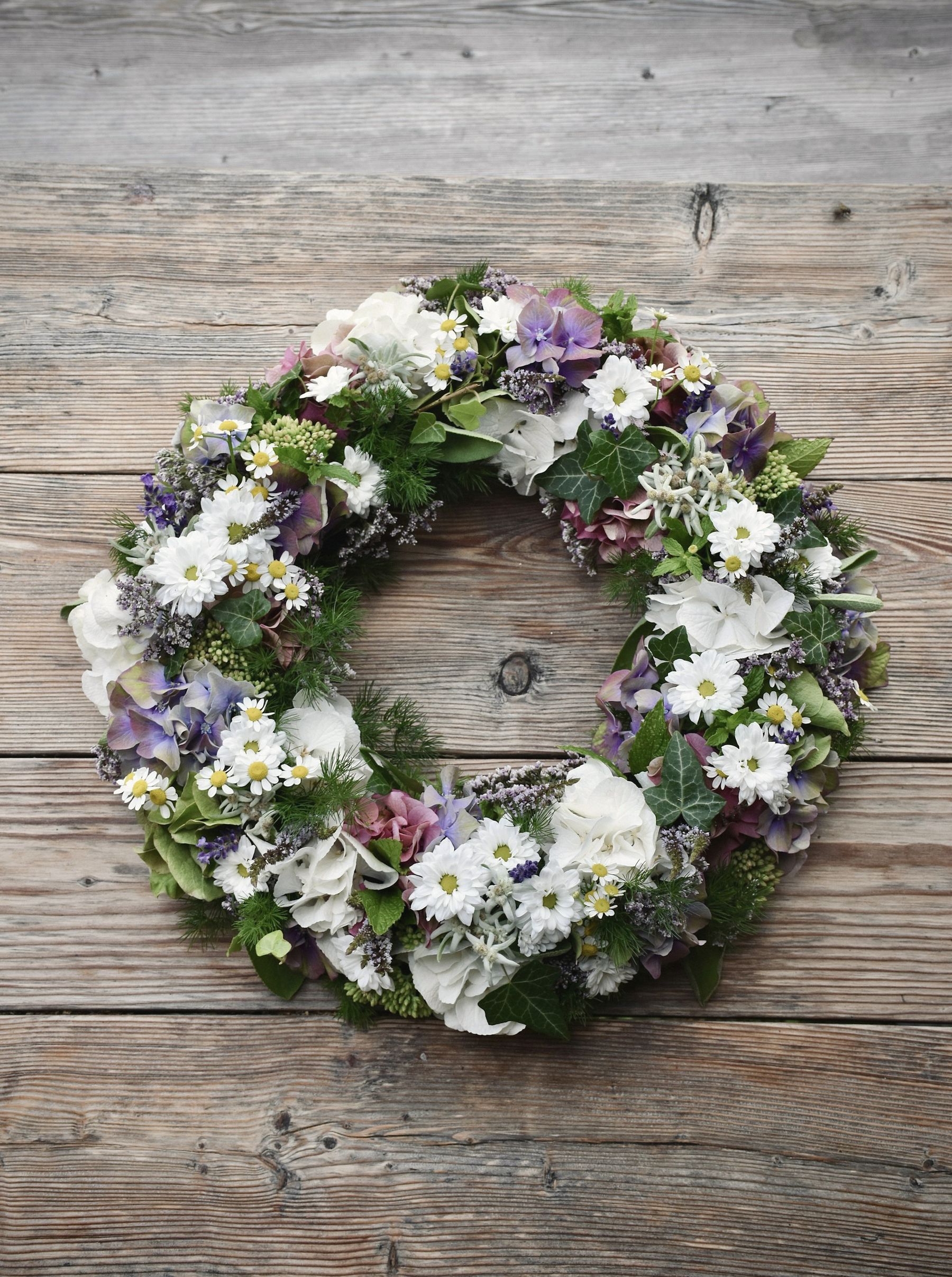A spring wreath of white and purple blooms on a weathered wood door