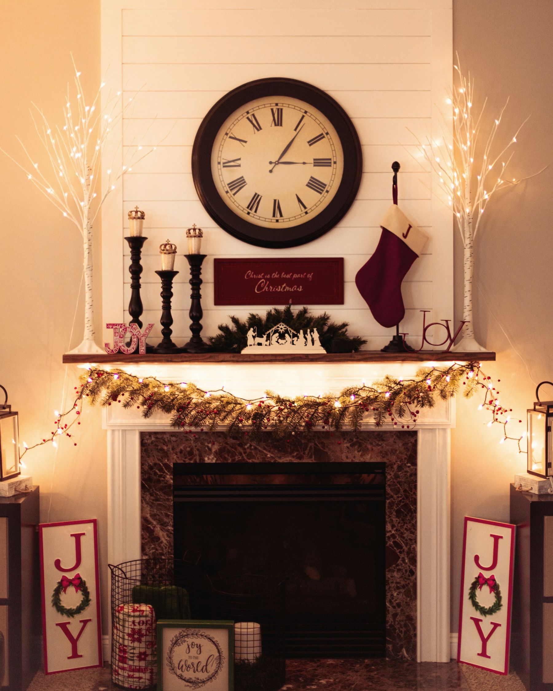 A glowing holiday mantel with garland, stockings and a large clock